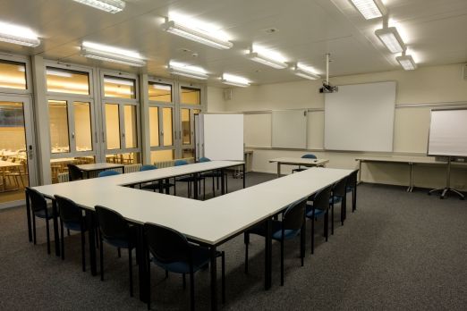 Heller Meetingraum mit U-förmiger Tischanordnung, Whiteboard und Projektion – ideal für Workshops und Schulungen in der Region Thunersee. ©Seaside Spiez Seminarraum mit U-Bestuhlung, Beamer und Leinwand in Thun