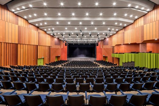Geräumiges, modernes Auditorium mit heller Beleuchtung, großzügigen Sitzreihen und einer zentralen Bühne. Die stilvolle Holzverkleidung und akustisch optimierten Wände schaffen das perfekte Ambiente für Tagungen, Firmenevents und Konferenzen am Thunersee – ideal für Unternehmen und Verbände, die eine professionelle Eventlocation suchen. Modernes Auditorium mit Bühne