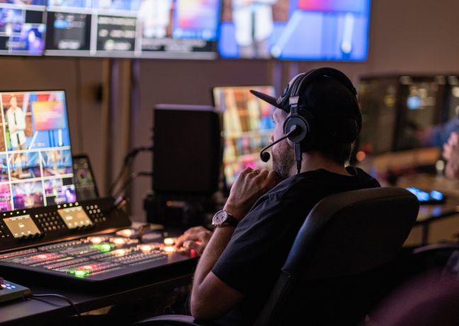 Techniker am Mischpult überwacht Monitore und Audio in der Regie – professionelle Live-Eventproduktion für Meetings und Konferenzen. ©KKThun Eventtechnik-Regie mit Ton- und Bildmischpult während einer Live-Produktion