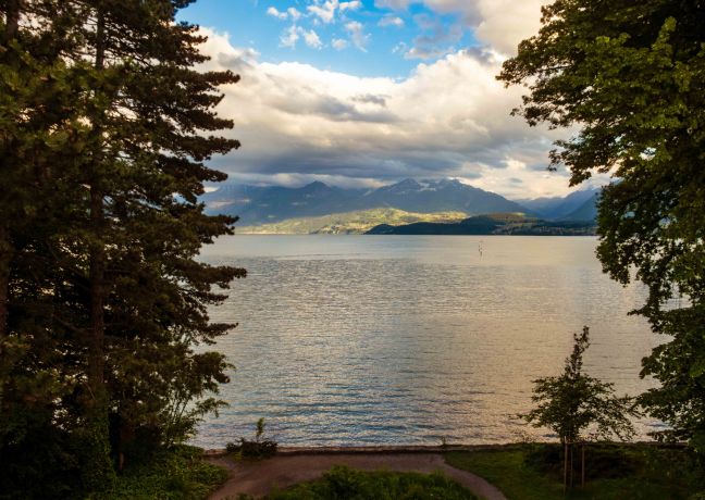 Beeindruckende Aussicht direkt vom Hotel auf den glitzernden Thunersee, eingerahmt von majestätischen Bergen und üppigen Bäumen. Perfekte Kulisse für inspirierende Geschäftsveranstaltungen, Meetings und Firmenevents in entspannter, naturnaher Atmosphäre am Wasser. Idyllischer Blick auf den Thunersee
