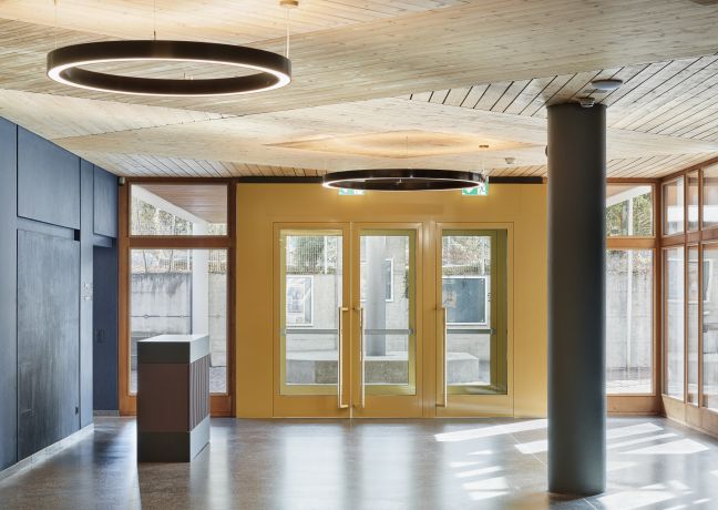 Helles Eingangsfoyer mit Ring-Deckenleuchten, Holdecke, Säule und grossen Glastüren – idealer Empfangsbereich für Business-Events in der Thunerseeregion. ©Gemeinde Spiez Modernes Foyer mit Holdecke, Ring-Leuchten und Glastüren in Thun
