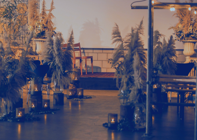 Stimmungsvolle Setup-Szene für Business-Events: Kerzen, Lampions und Trockenblumen arrangiert entlang eines Gangs in eleganter Location. ©Frachtraum Thun Stilvolle Event-Location mit Kerzenlicht und Trockenblumen-Dekor in warmem Abendlicht