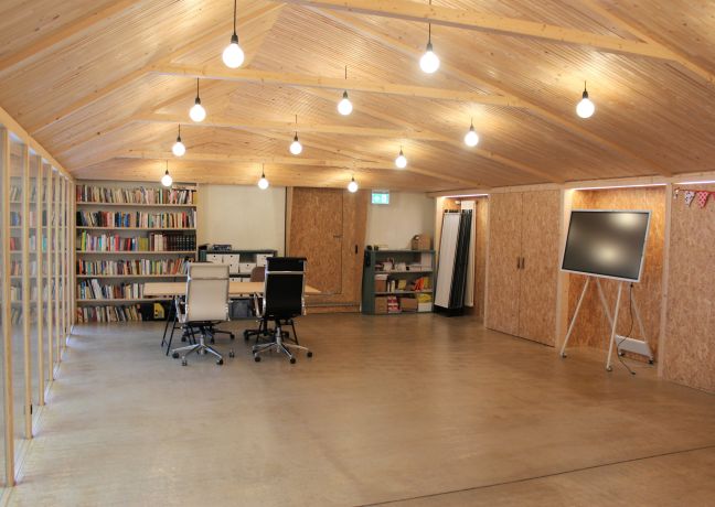 Heller Seminarraum mit Holzdecke, Bibliothek und Bildschirm in der Thunersee-Region