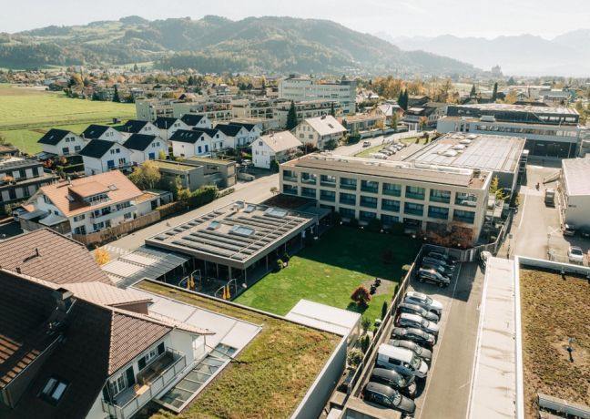 Luftaufnahme eines modernen Veranstaltungsgebäudes in Thun, eingebettet in eine idyllische Wohnumgebung mit Blick auf die Berner Alpen. Großzügige Grünflächen, Parkmöglichkeiten und klare Architektur schaffen ideale Voraussetzungen für Business-Events und Tagungen im Herzen des Berner Oberlands. ©Schützen Moderne Eventlocation mit Alpenblick
