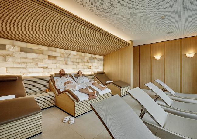 Entspannter Spa-Ruheraum mit Relaxliegen, Holzvertäfelung und Natursteinwand – ideal für eine erholsame Auszeit nach einem Event am Thunersee. ©Eden Spiez Ruheraum im Spa mit Liegen und warmem Holzdesign am Thunersee