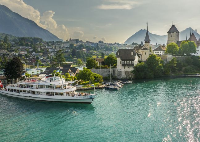 Ein Passagierschiff gleitet über den türkisfarbenen Thunersee; im Hintergrund Schloss Thun, die Altstadt und die Berner Alpen.
©BLS Schifffahrt Ausflugsschiff auf dem Thunersee vor Schloss Spiez und Alpenpanorama