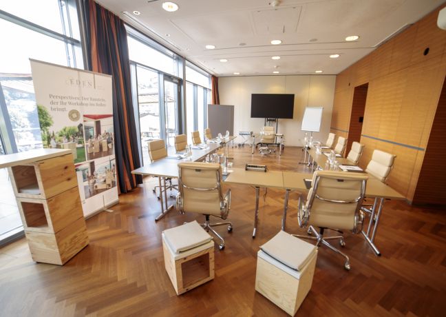 Moderner Meetingraum mit großen Fenstern, U-Form-Tischen, Whiteboard und Flipchart – ideal für Workshops und Tagungen am Thunersee. ©Eden Spiez Heller Seminarraum mit U-Form-Bestuhlung und Seeblick in der Region Thun-Thunersee