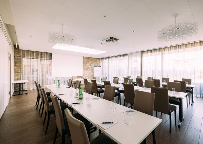 Heller, freundlich gestalteter Seminarraum mit großen Fenstern, modernen Stühlen und flexibler Tischanordnung. Die natürliche Beleuchtung schafft eine angenehme Arbeitsatmosphäre, optimal für Meetings, Workshops oder Firmenveranstaltungen am Thunersee. Perfekt geeignet für Business-Events jeder Größe. ©Schützen Stockhorn - Moderner Tagungsraum mit Tageslicht