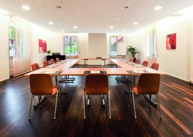 Moderner Meetingraum mit U-Form-Bestuhlung, grossen Fenstern und Kunst an den Wänden – ideal für Workshops und Seminare am Thunersee. ©Parkhotel, Gunten Heller Seminarraum mit U-Bestuhlung, Parkettboden und Tageslicht