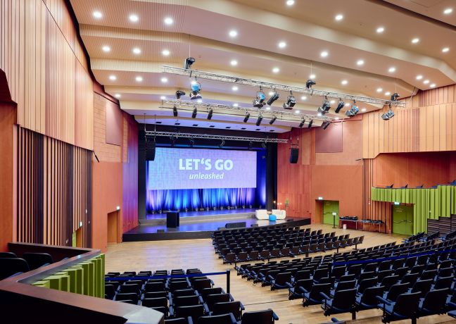 Grosszügiger Veranstaltungssaal mit Bühne, Leinwand und professioneller Technik – ideal für Kongresse, Tagungen und Firmenanlässe in der Thun-Thunersee Region. ©KKThun Moderner Kongresssaal mit Bühne, Lichttechnik und Reihenbestuhlung in Thun