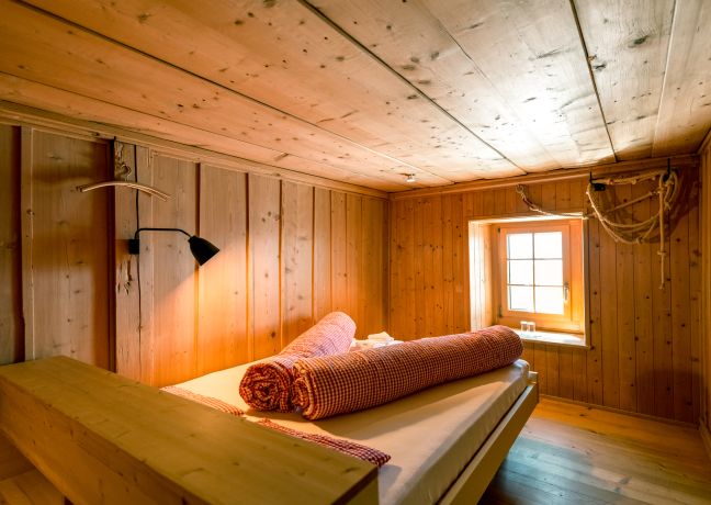 Rustikales Hotelzimmer aus Holz mit Doppelbett und Fenster