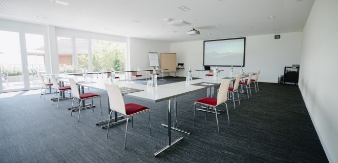 A bright, U-shaped seminar room with a projector and natural light in the Lake Thun region