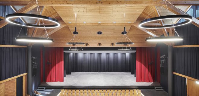 Moderner Veranstaltungssaal mit Bühne, Reihenbestuhlung und Ringlichtern in Thun