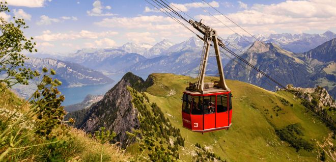 A red cable car gliding over green mountain slopes with a view of Lake Thun