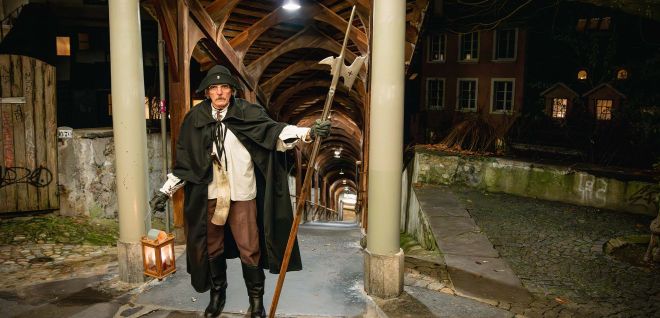 Night watchman with lantern under a covered wooden walkway in Thun