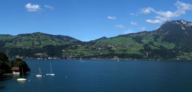 Blick über den Thunersee mit Segelbooten und Alpenpanorama bei blauem Himmel