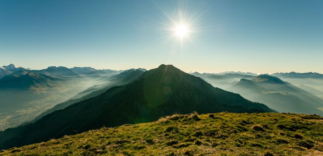 Sonnenaufgang über Alpenpanorama bei Thunersee mit grüner Bergwiese im Vordergrund