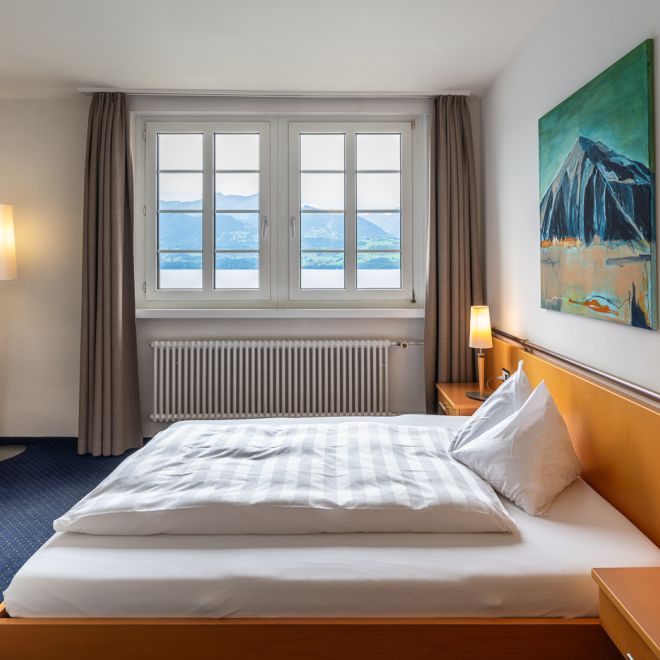 A bright hotel room with a double bed and views of Lake Thun and the mountains