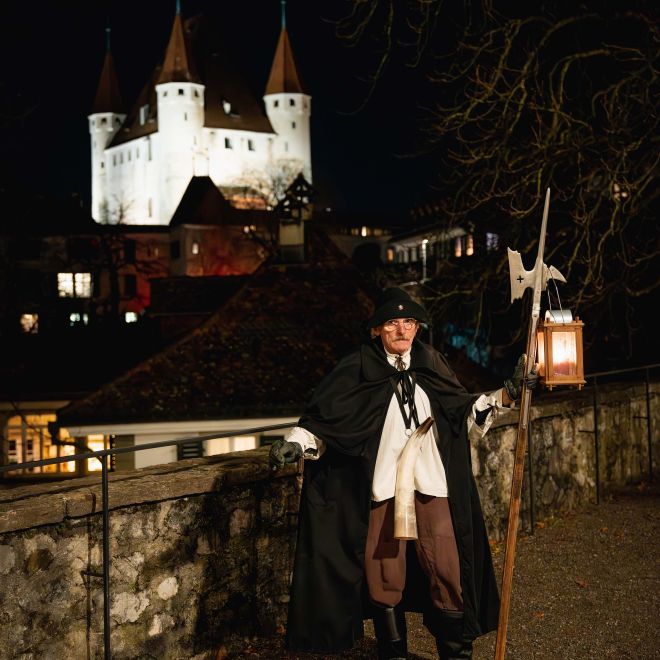 A night watchman in historical costume outside Thun Castle at night