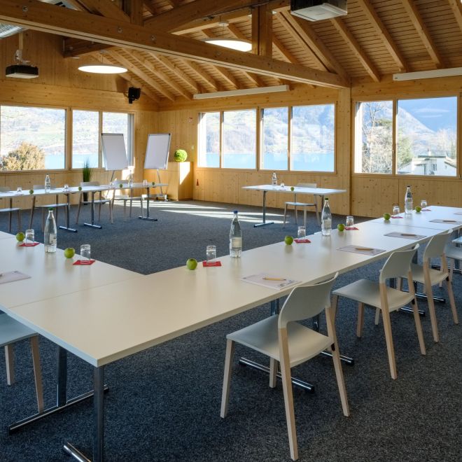 A bright seminar room with U-shaped seating and views of the mountains by Lake Thun