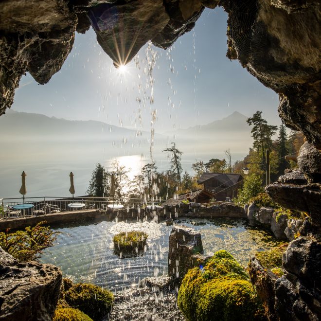 Blick aus einer Höhle auf den Thunersee mit Wasserfall und Morgensonne